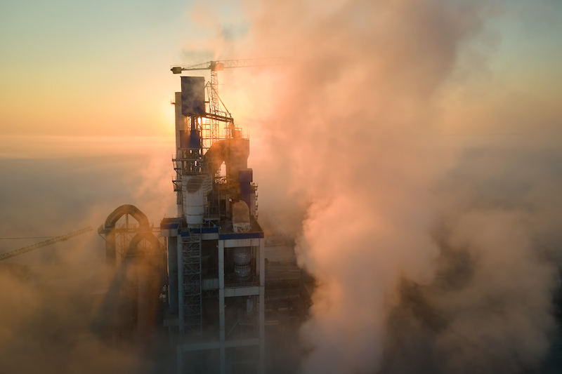 Aerial view of cement factory with high concrete plant structure and tower crane at industrial manufacturing site on foggy evening. Production and global industry concept.